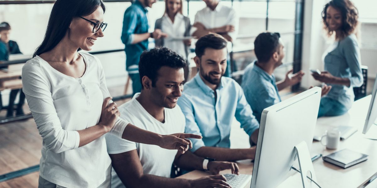 Young Smiling Business People Working in Office. Group of Young Coworkers Sitting Together at Table and Working on Laptops in Modern Office. Teamwork Concept. Corporate Lifestyle
