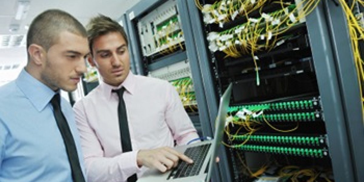 two people looking at laptop in front of a large server